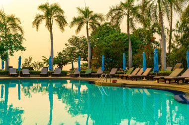 Gün batımında yüzme havuzunda şemsiyeli plaj sandalyesi ya da bilardo yatağı