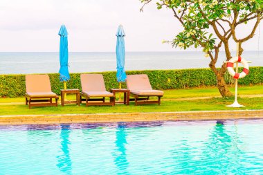 Sandalye havuzu ve şemsiyeyle okyanus arka planında yüzme havuzu