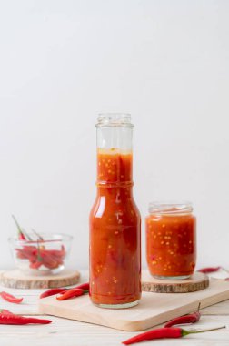 Şişede kırmızı biber ya da kırmızı biber sosu ve arka planda kavanoz.