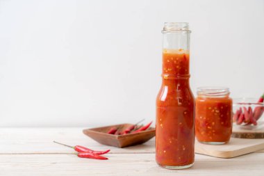 Şişede kırmızı biber ya da kırmızı biber sosu ve arka planda kavanoz.