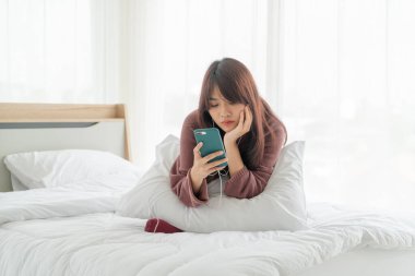 Güzel Asyalı kadınlar yatakta akıllı telefon oynuyorlar.