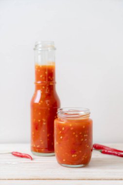 Şişede kırmızı biber ya da kırmızı biber sosu ve arka planda kavanoz.