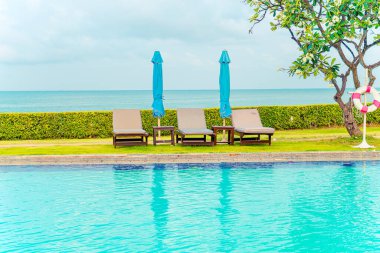 Sandalye havuzu ve şemsiyeyle okyanus arka planında yüzme havuzu