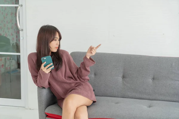 Güzel Asyalı Kadın Oturma Odasındaki Gri Koltukta Akıllı Telefon Kullanıyor — Stok fotoğraf