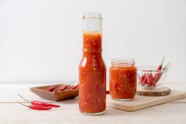 Şişede kırmızı biber ya da kırmızı biber sosu ve arka planda kavanoz.