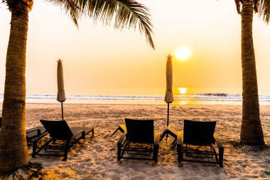 Güneş doğarken palmiye ağacı ve deniz plajı olan şemsiye koltuğu plajı - tatil ve tatil konsepti