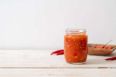 Şişede kırmızı biber ya da kırmızı biber sosu ve arka planda kavanoz.