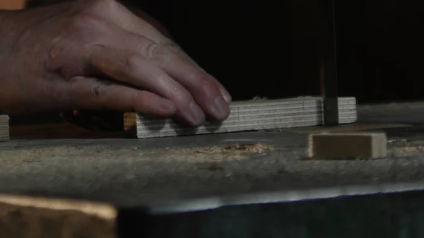 Perto em mãos de carpinteiro que corta um pedaço de madeira com uma serra de fita — Fotografia de Stock