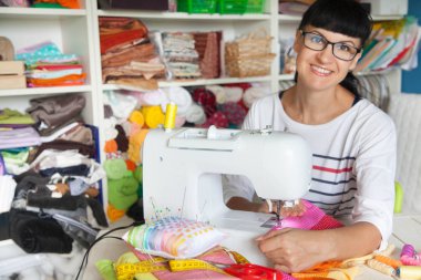 Bir dikiş makinesi yanında mutlu gülümseyen kadın. Kumaş, iplik ve 