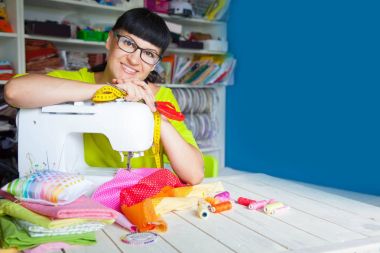 Bir dikiş makinesi yanında mutlu gülümseyen kadın. Kumaş, iplik ve 