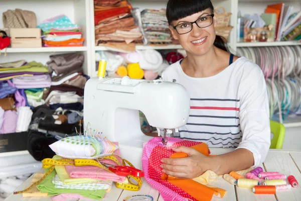 Bir dikiş makinesi yanında mutlu gülümseyen kadın. Kumaş, iplik ve 