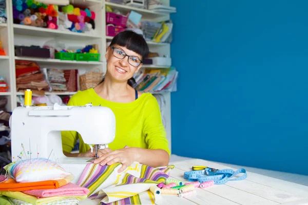Bir dikiş makinesi yanında mutlu gülümseyen kadın. Kumaş, iplik ve 
