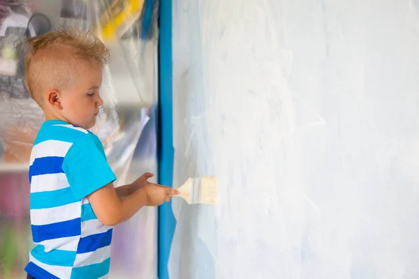 Il bambino dipinge la parete blu con un rullo. Il ragazzo tiene un la — Foto Stock