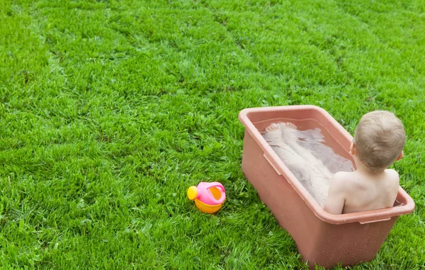 Yeşil çimenlerin üzerinde banyoda küçük çocuk yıkar. 4-5 / çocuk