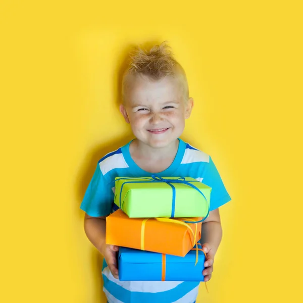 Il bambino tiene regali lucenti. Un ragazzo con un dono su una festa gialla — Foto Stock