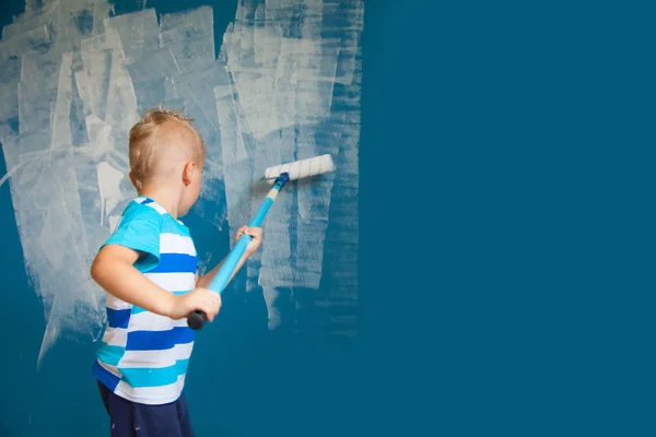 A criança pinta a parede azul com um rolo. O menino segura a la — Fotografia de Stock
