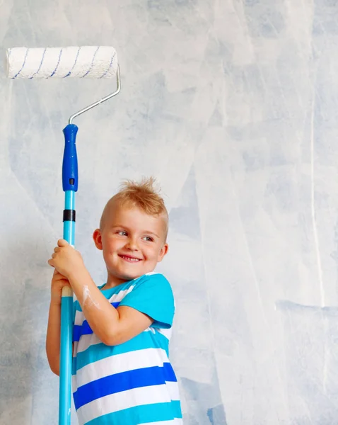 Il bambino dipinge la parete blu con un rullo. Il ragazzo tiene un la — Foto Stock