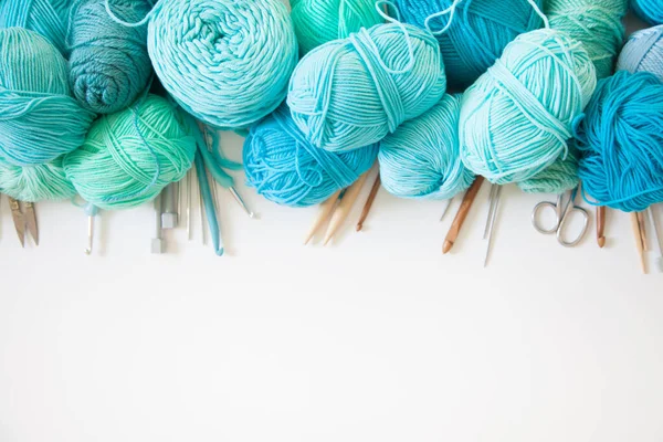 Pastel colored yarn in white basket and wooden crochet hooks of