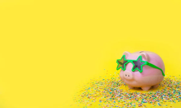 A pink piggy bank in fun green glasses at a party. Yellow backgr — Stok fotoğraf