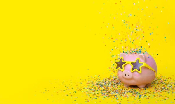 A pink piggy bank in fun glasses at a party and confetti. Yellow — Stok fotoğraf