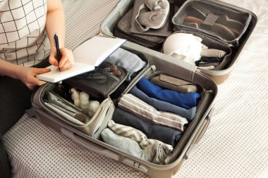 Kadın eli bavul hazırlıyor. Yatakta, yakın plan. Açık bavuldaki plaj aksesuarları. Seyahat çantası, farklı kıyafetler..