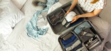 Kadın eli bavul hazırlıyor. Yatakta, yakın plan. Açık bavuldaki plaj aksesuarları. Seyahat çantası, farklı kıyafetler..