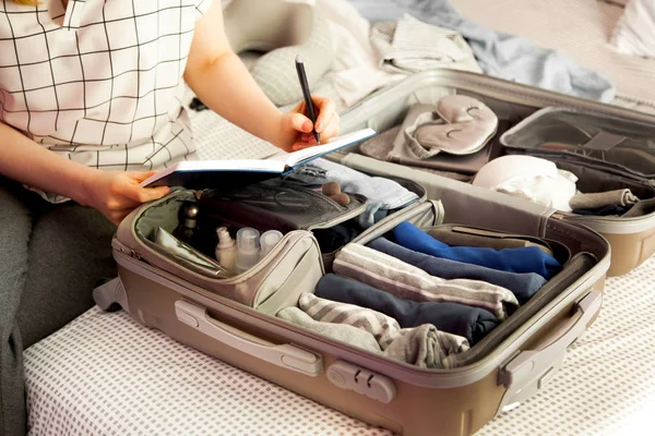 女性手在床上抱着旅行箱 特写镜头 海滩配件在打开的行李箱 旅行的车轮袋 不同的衣服 — 图库照片