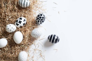 Farklı boyutlarda, altın ve siyah-beyaz geometrik desenlerle boyanmış güzel yumurtalar samanlıkta, izole edilmiş beyaz bir zeminde yatıyor. Paskalya toplantısı konsepti. Reklam alanı