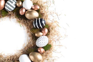 Altın ve geometrik siyaha boyanmış farklı boyutlarda yumurtalarla izole edilmiş beyaz bir zemin üzerinde uzanan sarı saman yuvasından üst çerçeve. Paskalya temalı selamlama teması. Kopyalama alanı