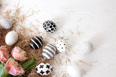 Üst manzara güzel altın ve siyah beyaz paskalya yumurtaları saman ve pembe püsküllü lalelerin yanında beyaz ahşap bir masanın üzerinde yatar. Güzel bir paskalya konsepti. Bahar kartı. Kopyalama alanı
