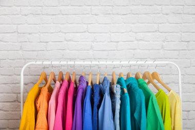 Kadın kıyafetleri tişörtleri ve bluzları beyaz tuğla duvara karşı gökkuşağının tüm renklerini sırasıyla tahta omuzlara asar. Gardıroptaki konsept güncellemesi. Reklam alanı