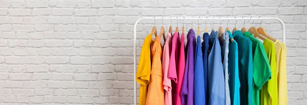 Women\'s wardrobe sweatshirts shirts and blouses hang on wooden shoulders in the order of all the colors of the rainbow against white brick wall. Concept update in the wardrobe. Advertising space