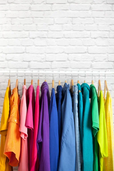 Wardrobe of womens clothing blouses and shirts hang on hangers in the order of colors of the rainbow on the background of brick wall.