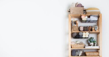 Ahşap askılar, iplik kumaşlı sepetler ve dikiş aksesuarları ve dikiş makinesi bir terzi atölyesinde beyaz arka planda duruyor. Temiz iş yeri ve özel dikiş kavramı. Kopyalama alanı