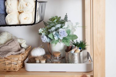 Farklı renkte iplikçiklerin ve aksesuarların üst görüntüsü evdeki terzi odasındaki ahşap bir rafın rafındaki çiçek saksısının yanında. Temizlik ve düzenlilik kavramı