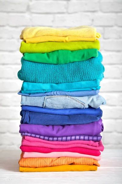 Women's wardrobe sweatshirts shirts and blouses hang on wooden shoulders in the order of all the colors of the rainbow against white brick wall. Concept update in the wardrobe. Advertising space