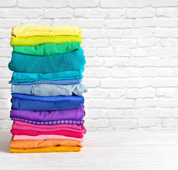 Women\'s wardrobe sweatshirts shirts and blouses hang on wooden shoulders in the order of all the colors of the rainbow against white brick wall. Concept update in the wardrobe. Advertising space