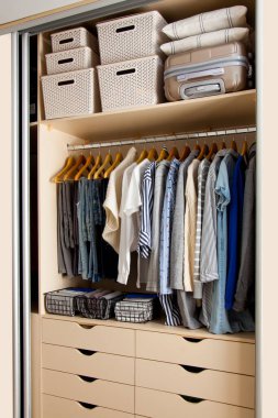 Wardrobe with perfect order clothes in blue and light shades on the hangers and things in containers. The concept of organizers and cleanliness in the house clipart