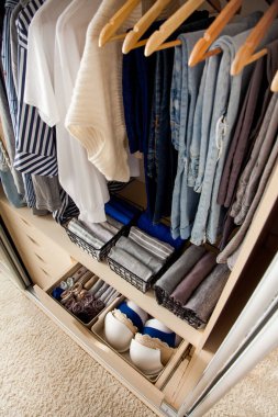 Düzgünce katlanmış şeylerin ve aksesuarların geniş bir gardıroptaki askıların altında asılı duran şeylerin üst görüntüsü. Doğruluk kavramı ve evdeki genel temizlik