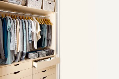 Wardrobe with perfect order clothes in blue and light shades on the hangers and things in containers. The concept of organizers and cleanliness in the house clipart