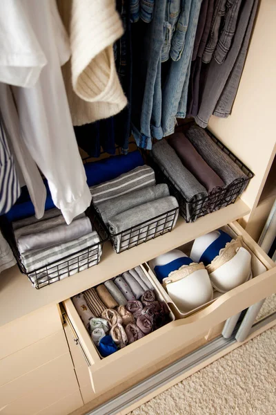 Top view of neatly folded things and accessories in boxes and drawers lying under things hanging on hangers in a large wardrobe. Concept of accuracy and general cleaning in the house