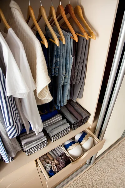Top view of neatly folded things and accessories in boxes and drawers lying under things hanging on hangers in a large wardrobe. Concept of accuracy and general cleaning in the house