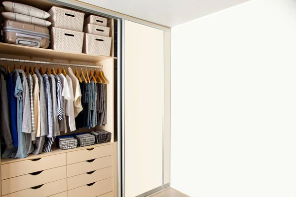 Wardrobe with perfect order clothes in blue and light shades on the hangers and things in containers. The concept of organizers and cleanliness in the house