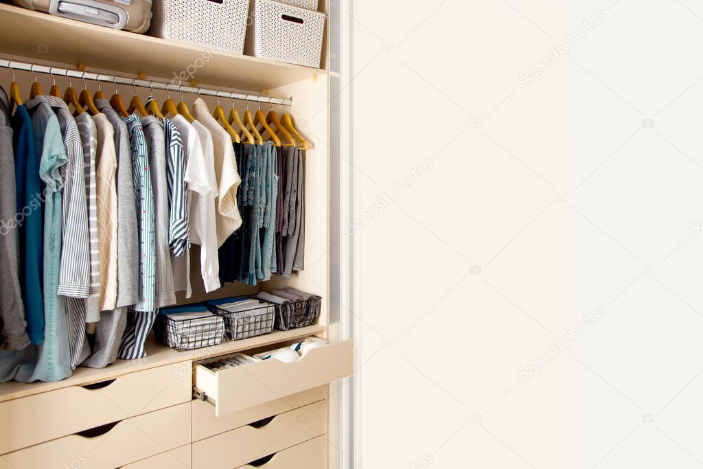 Wardrobe with perfect order clothes in blue and light shades on the hangers and things in containers. The concept of organizers and cleanliness in the house