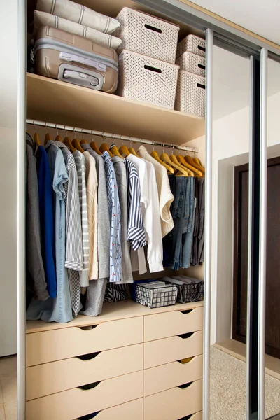 Wardrobe with perfect order clothes in blue and light shades on the hangers and things in containers. The concept of organizers and cleanliness in the house