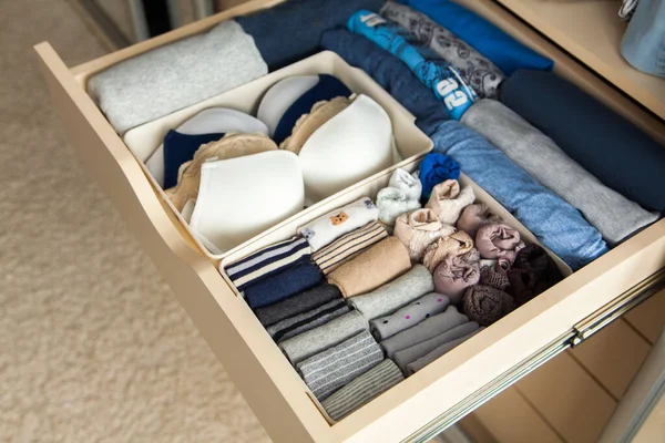 Top view of neatly folded things in grey blue color and accessories are in a drawer in the closet. The concept of perfect tidy and convenient storage of clothes