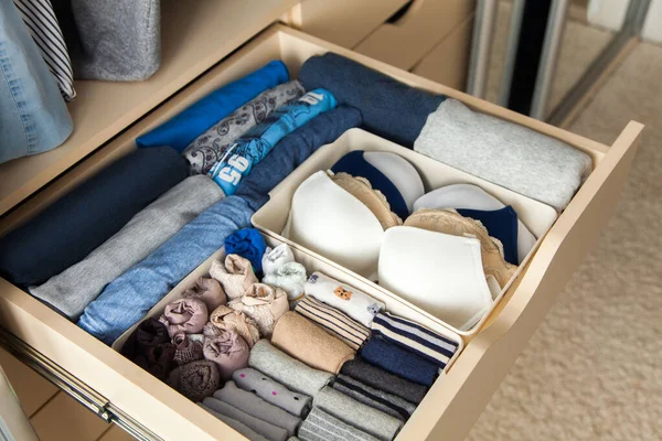 Top view of neatly folded things in grey blue color and accessories are in a drawer in the closet. The concept of perfect tidy and convenient storage of clothes