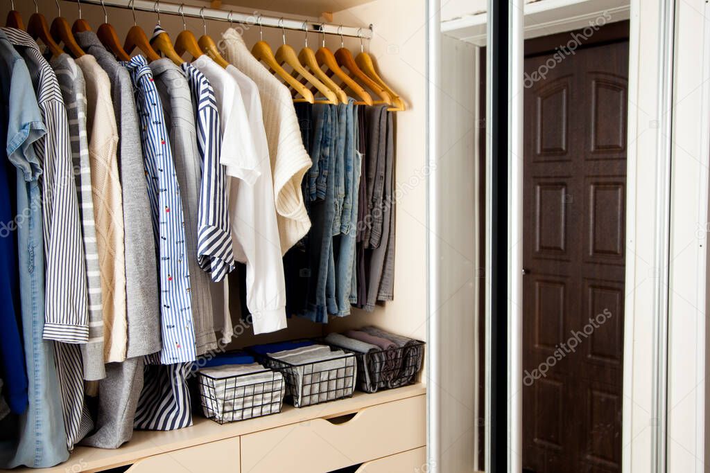 Wardrobe with perfect order clothes in blue and light shades on the hangers and things in containers. The concept of organizers and cleanliness in the hous