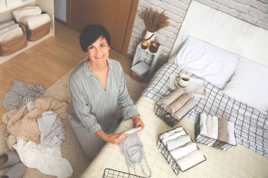 Güzel, genç, esmer bir kadının rahat yatak odasında otururken bir şeyleri örgü metal kaplar üzerinde katlamasının en güzel görüntüsü. Haftalık temizlik konsepti