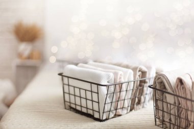 Beyaz kıyafetlerin ve keten kumaşların yatak odasındaki ağlı metal kaplarda düzgünce katlanmış ve bulanık yatağın arka planında. Mükemmel organizasyon kavramı. Reklam alanı